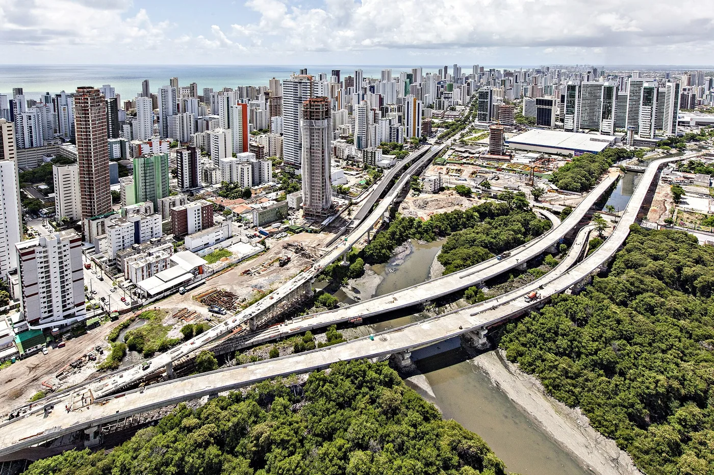 Vista aérea de manguezal cortado por viadutos, com prédios altos ao fundo, no Recife