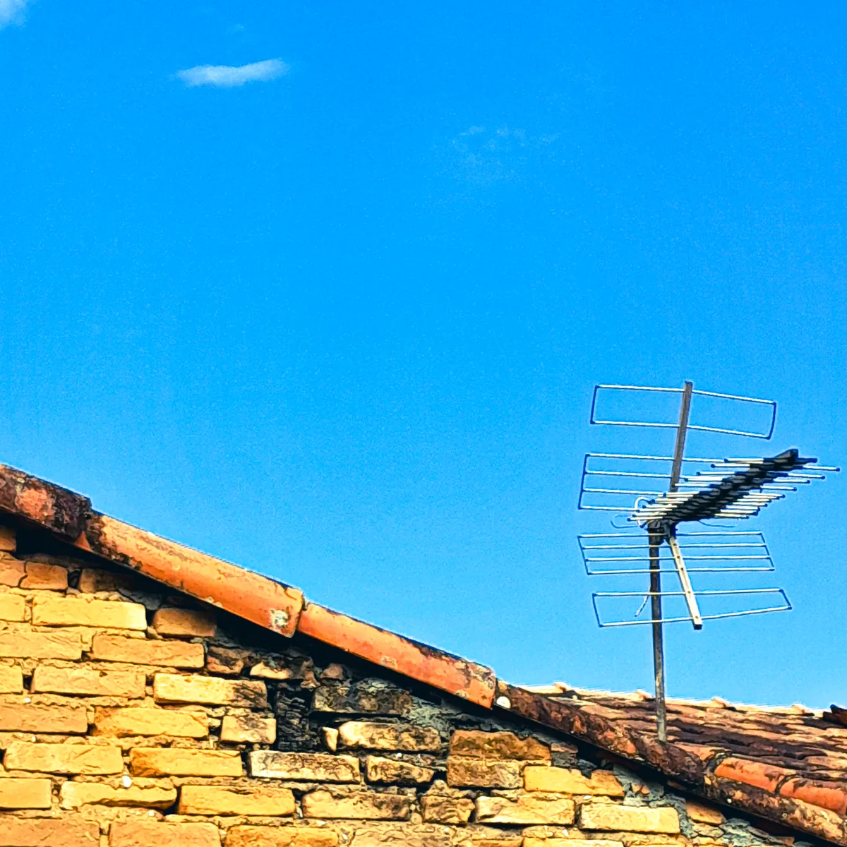 Muro de tijolo com uma antena de TV contra o céu azul: capa da Antena Ligada, a rádio da LUMENAR
